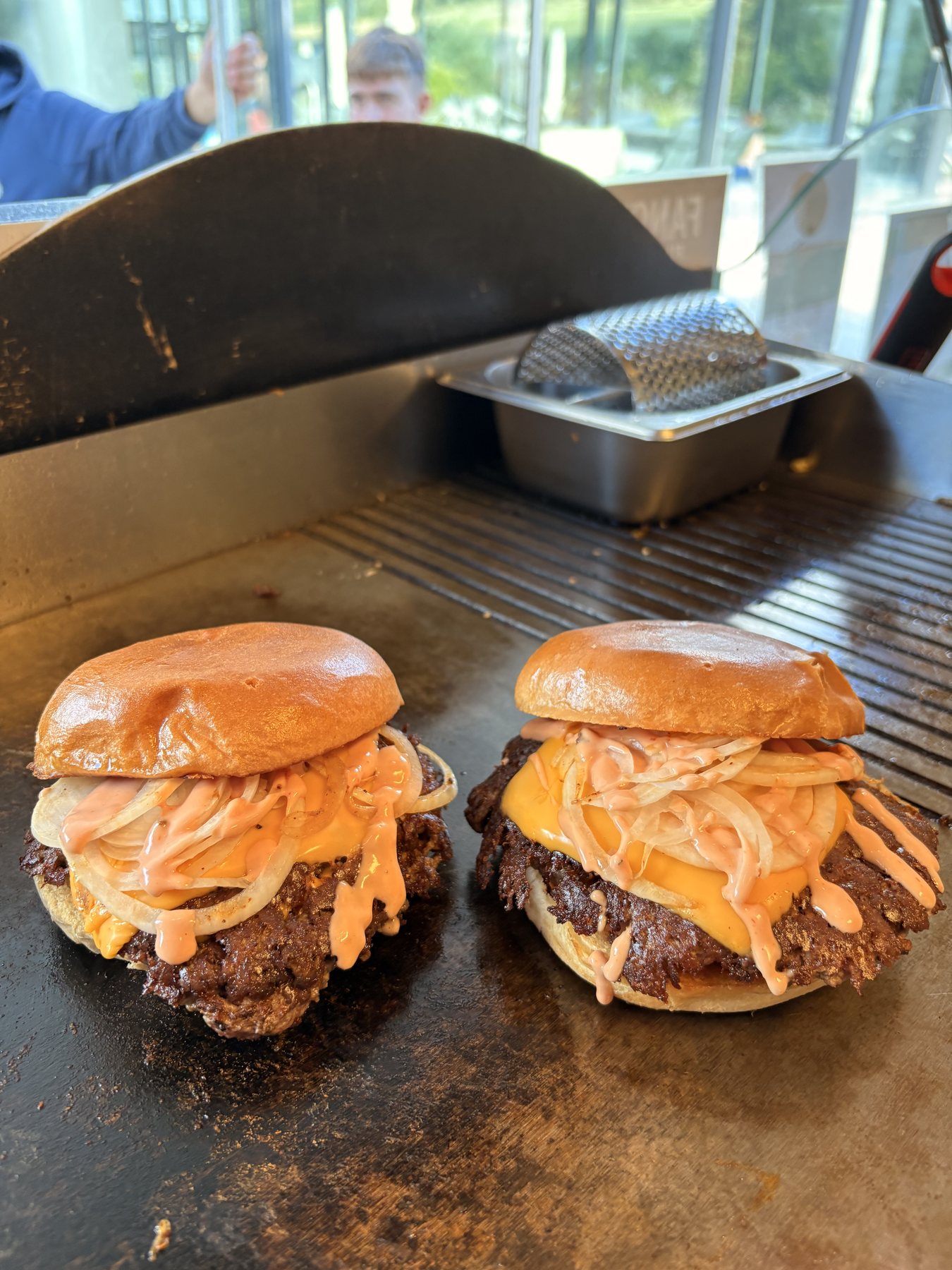 Zwei frisch gesmashte Fancy's Burger mit Zwiebeln, Käse und Sauce auf der heißen Griddle des Food Trucks