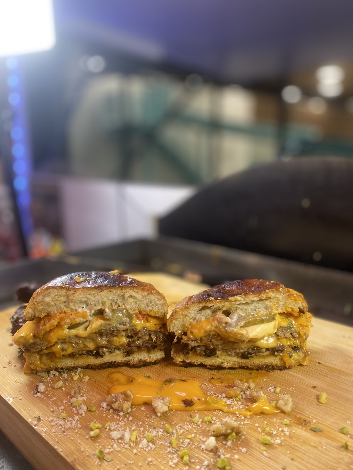 Aufgeschnittener Burger mit zwei Patties, laufendem Käse und Gurken auf einem Holzbrett