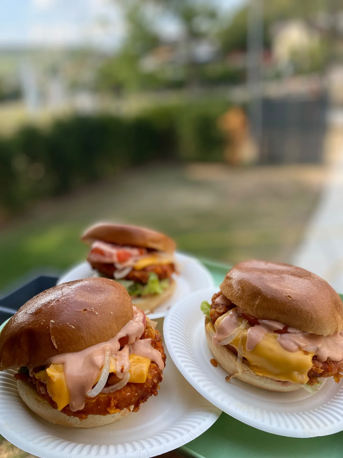 Drei Chicken Burger mit knuspriger Panade, Käse, Gemüse und Sauce auf einem Tisch
